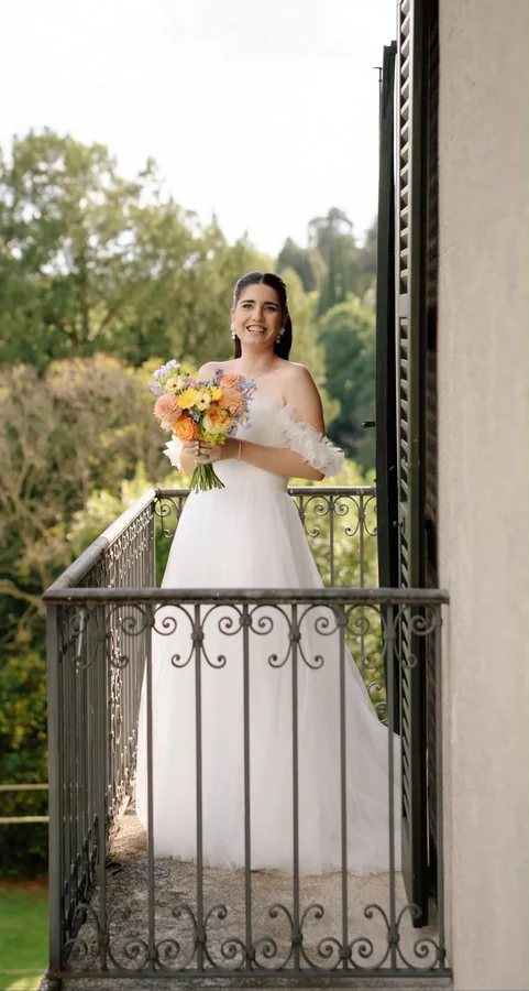 Sposa con bouquet colorato affacciata a un balcone in ferro battuto.