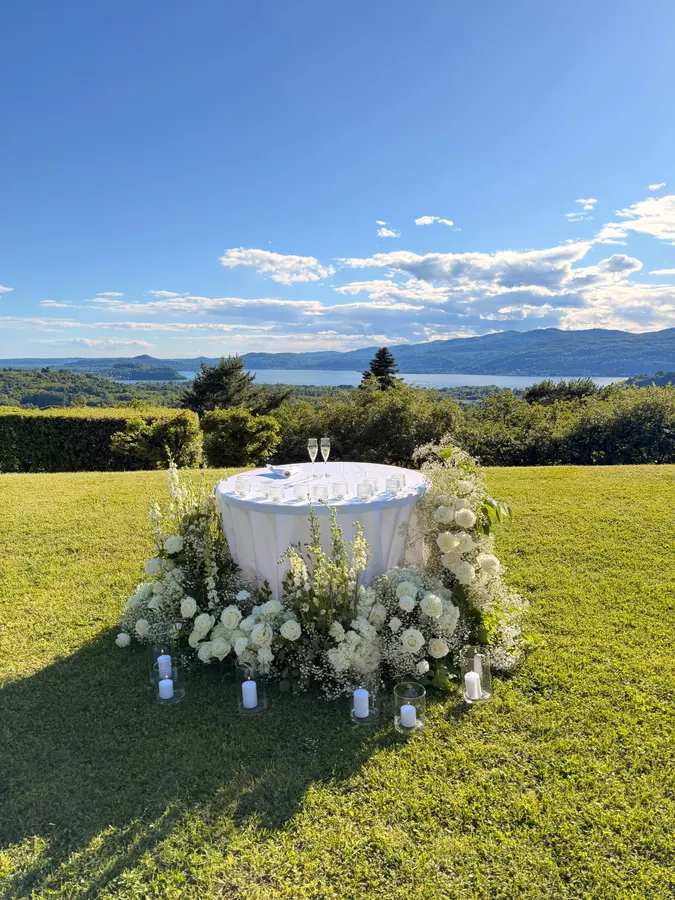 Tavolo del ricevimento su un prato, con composizione floreale bianca