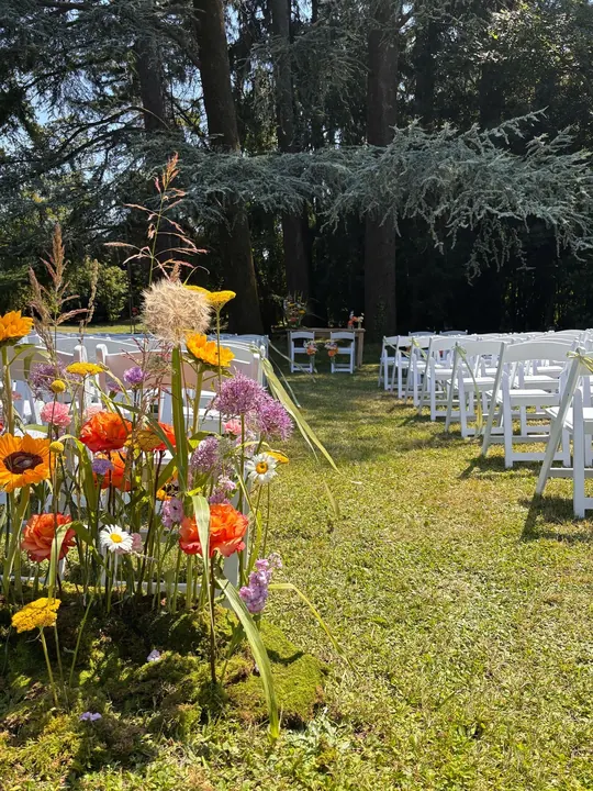 Allestimento floreale della cerimonia all'aperto tra file di sedie bianche